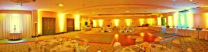 Large banquet hall set up for an event with round tables, chairs, and warm yellow lighting.