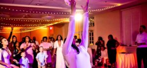 A bride in white throws her bouquet as guests watch and reach to catch it in a warmly lit reception hall.
