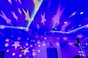 Blue-lit room with white star-shaped light projections on the walls and ceiling, with several spotlights visible.