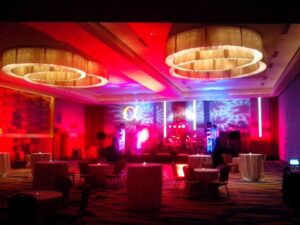 Ballroom with round tables, chairs, and vibrant red lighting, featuring a stage set up for a live performance.