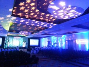 Conference room with rows of chairs, stage, and star-shaped ceiling lights creating a blue and white glow.